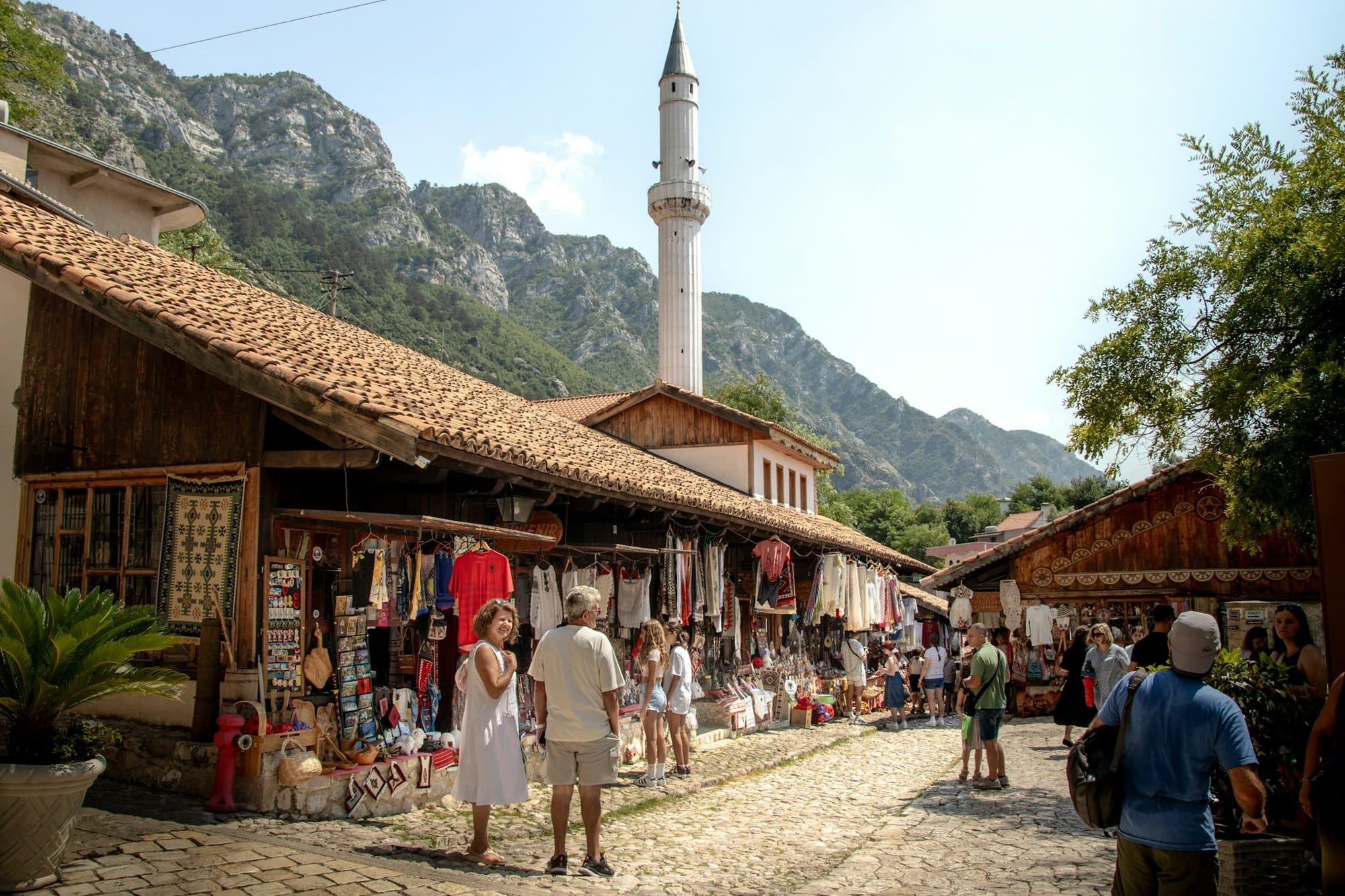 Visitors browsing the old bazaar in Krujë, with the minaret and mountains behind